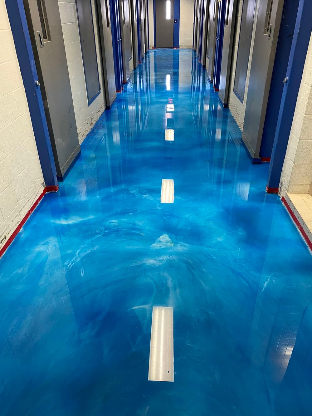 Vibrant blue epoxy floor in a hallway with metal doors and bright overhead lights.