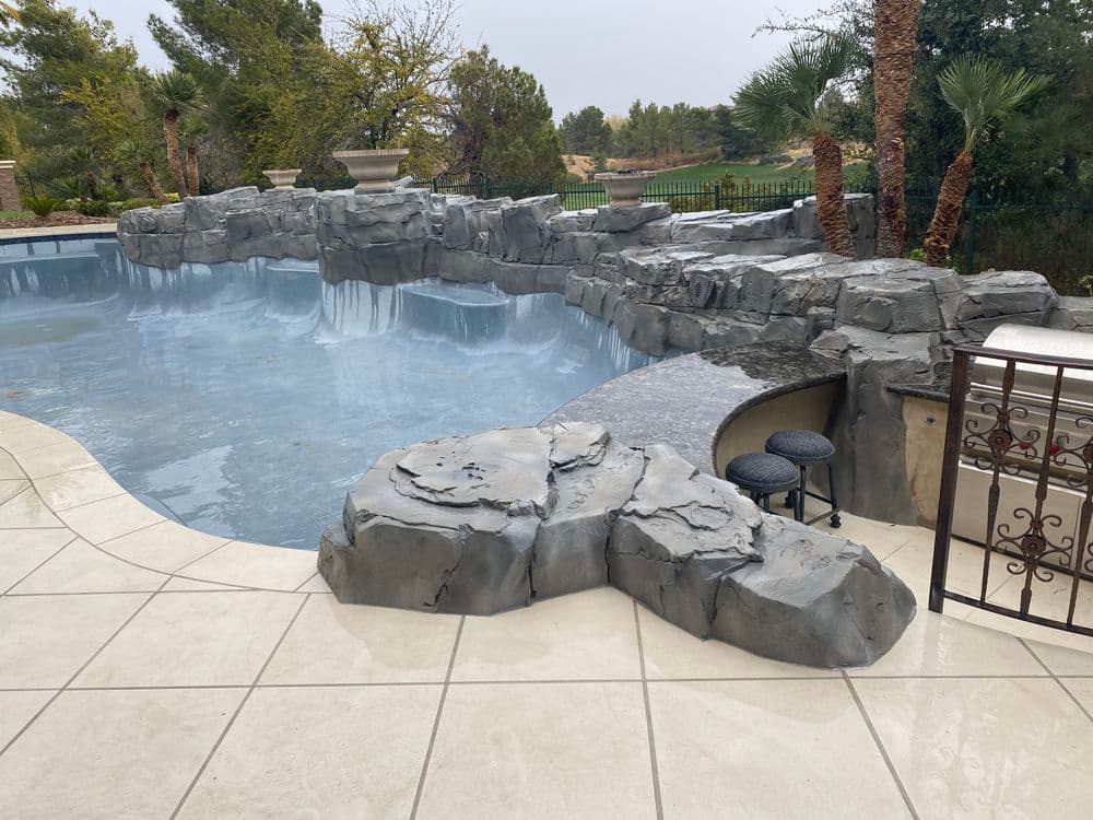 Luxury pool with rock formation, wet tiles, and landscaped greenery in the background.