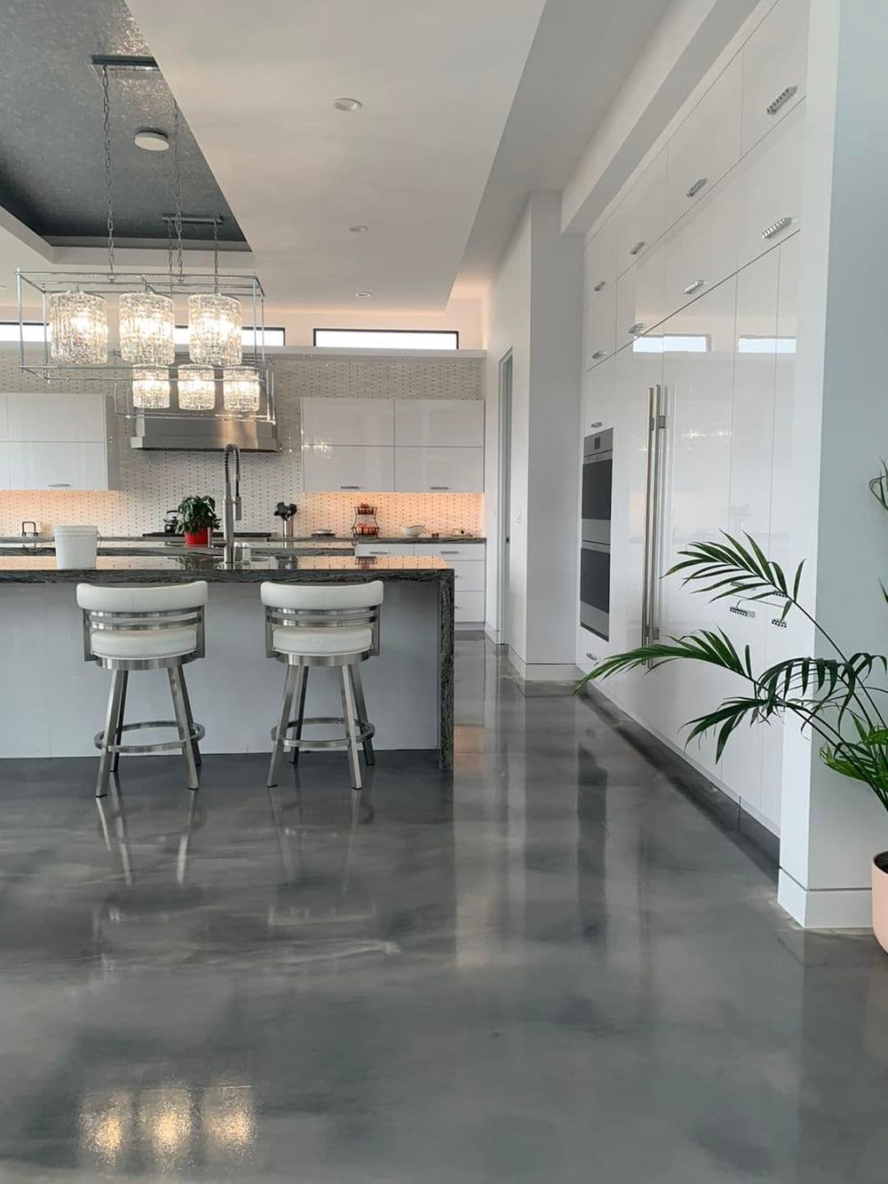 Modern kitchen interior with sleek white cabinetry, stone counters, and contemporary bar stools.